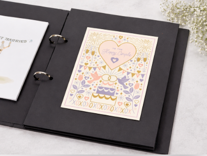 Black photo album with a decorative card featuring a heart and floral designs on a light surface.